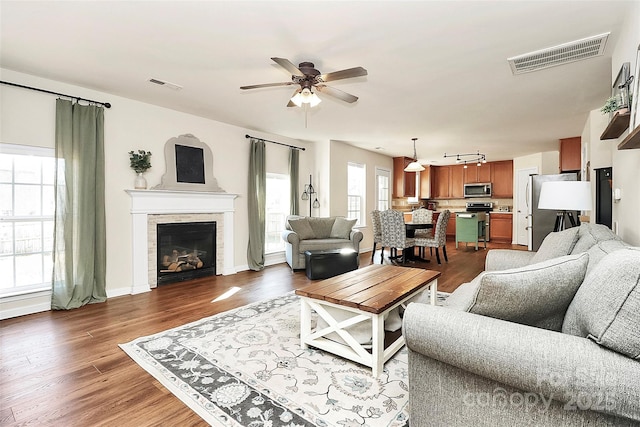 living room with dark wood-style flooring, visible vents, a fireplace, and ceiling fan