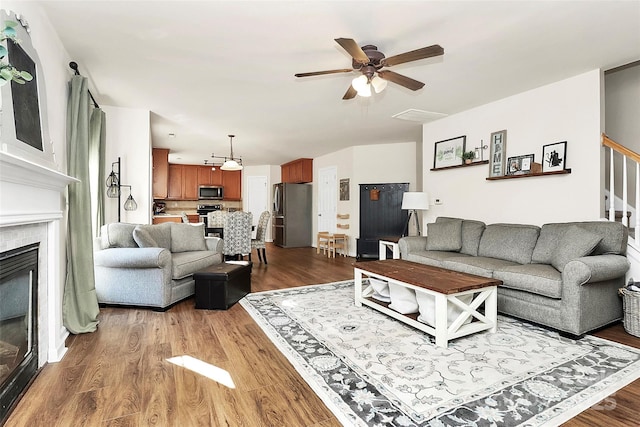 living room featuring stairs, a ceiling fan, a fireplace, and wood finished floors