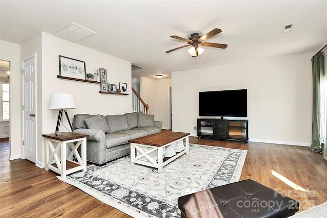 living room featuring visible vents, ceiling fan, stairway, and wood finished floors