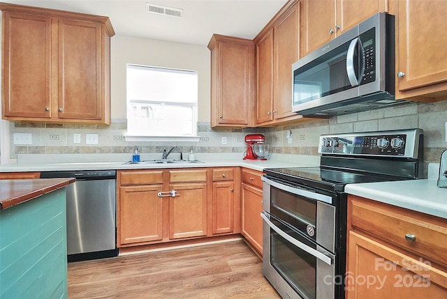 kitchen featuring stainless steel appliances, light countertops, brown cabinets, and visible vents