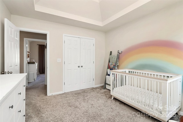 bedroom with a closet, a raised ceiling, light colored carpet, a crib, and baseboards