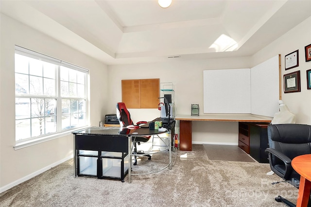 office space featuring baseboards, visible vents, a tray ceiling, and light colored carpet