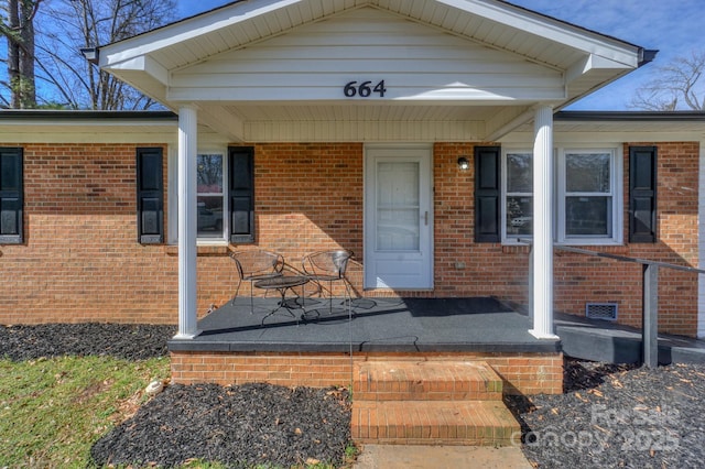 entrance to property with a porch, crawl space, and brick siding