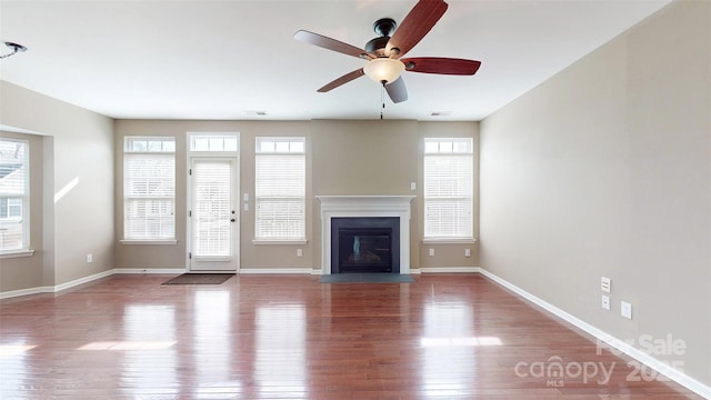 unfurnished living room with a fireplace with flush hearth, a wealth of natural light, visible vents, and wood finished floors