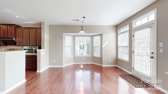 kitchen with light wood finished floors, visible vents, stainless steel microwave, decorative light fixtures, and a healthy amount of sunlight