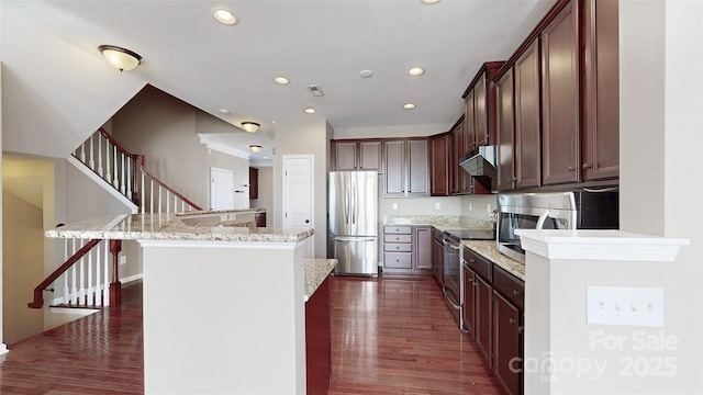 kitchen with light stone counters, dark wood-style floors, stainless steel appliances, a kitchen island, and under cabinet range hood