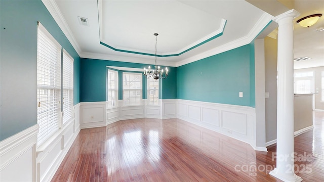 unfurnished room featuring visible vents, a raised ceiling, decorative columns, and light wood-style floors