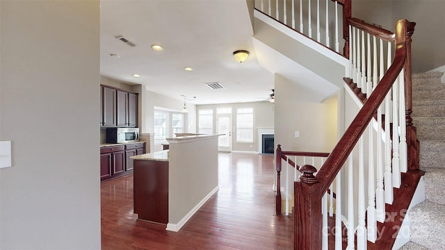 interior space featuring a fireplace, visible vents, open floor plan, dark wood-style floors, and stainless steel microwave