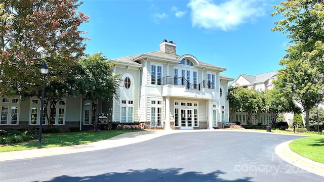 view of front of home with french doors, a chimney, and a front lawn