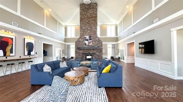 living room with visible vents, a decorative wall, dark wood-type flooring, and a stone fireplace