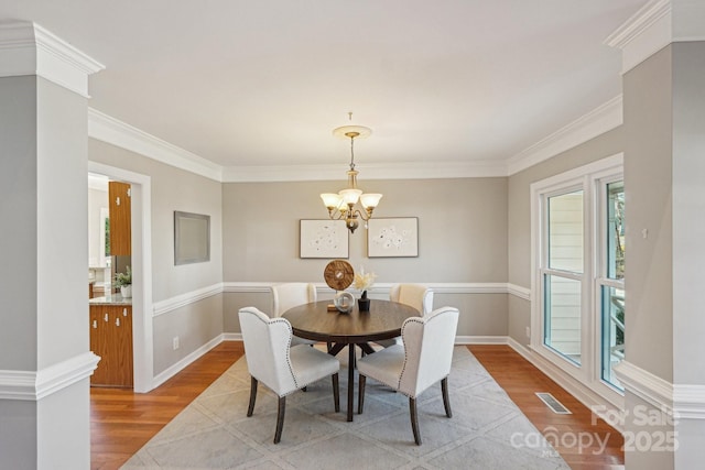 dining space featuring crown molding, light wood-type flooring, visible vents, and an inviting chandelier