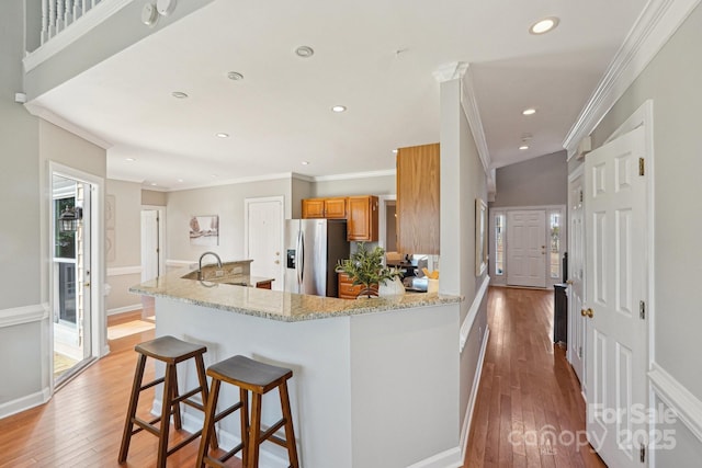 kitchen featuring light stone counters, a breakfast bar area, light wood-type flooring, brown cabinets, and stainless steel fridge