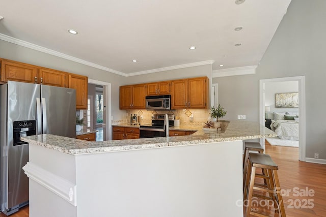 kitchen featuring light wood-style flooring, stainless steel appliances, a kitchen breakfast bar, decorative backsplash, and brown cabinets