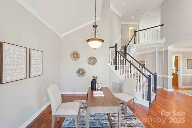 dining space with a high ceiling, wood finished floors, baseboards, stairway, and crown molding