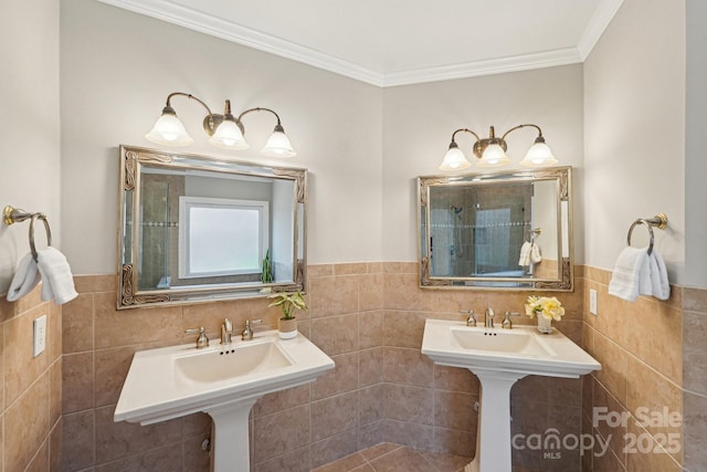 bathroom with a wainscoted wall, ornamental molding, two sinks, and tile walls