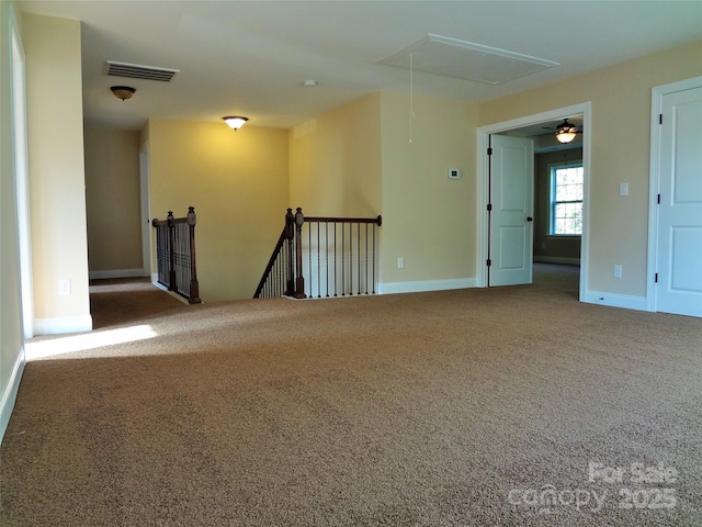 carpeted empty room featuring visible vents, attic access, and baseboards