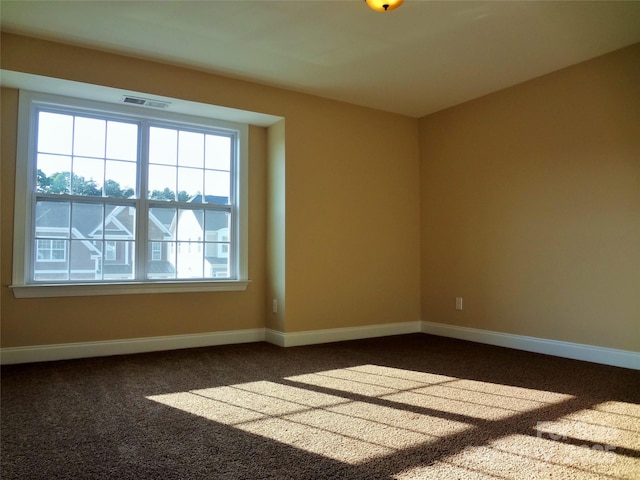 unfurnished room with dark carpet, visible vents, and baseboards