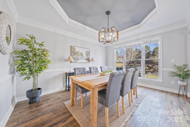 dining area featuring crown molding, a tray ceiling, wood-type flooring, and a notable chandelier