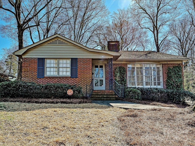 view of front facade featuring brick siding, a chimney, and a front lawn