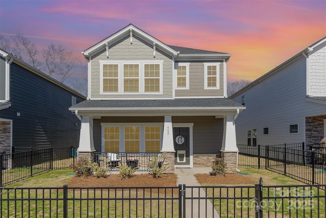 craftsman-style home with a porch, a fenced front yard, a shingled roof, stone siding, and a front lawn