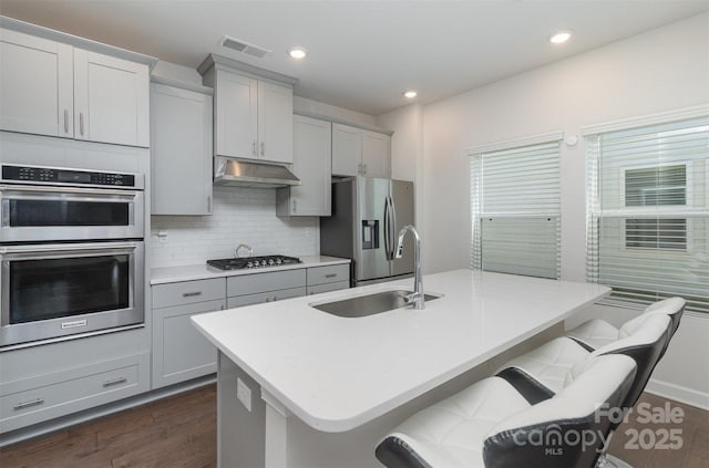 kitchen with tasteful backsplash, visible vents, stainless steel appliances, under cabinet range hood, and a sink