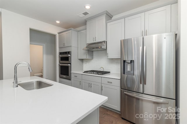 kitchen featuring decorative backsplash, appliances with stainless steel finishes, light countertops, under cabinet range hood, and a sink