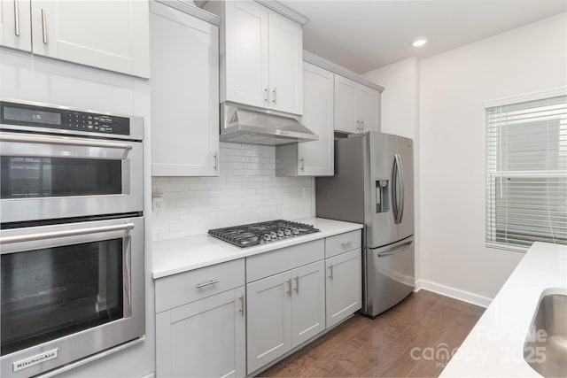 kitchen with under cabinet range hood, stainless steel appliances, dark wood-type flooring, light countertops, and decorative backsplash