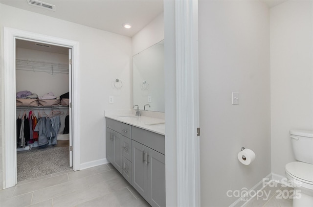 full bathroom featuring double vanity, visible vents, a spacious closet, toilet, and a sink