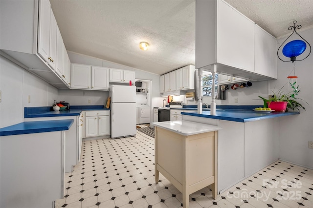 kitchen featuring a peninsula, vaulted ceiling, freestanding refrigerator, light floors, and washer and clothes dryer