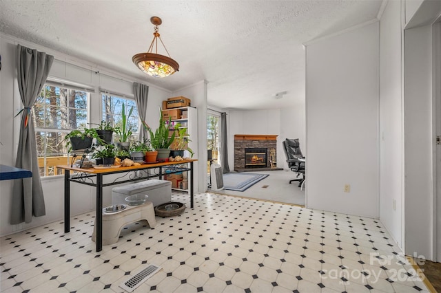 interior space with a textured ceiling, a stone fireplace, crown molding, and tile patterned floors