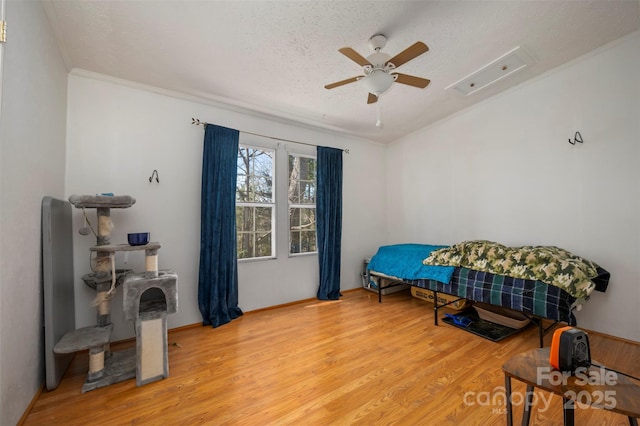 bedroom with a textured ceiling, ornamental molding, light wood-type flooring, and a ceiling fan