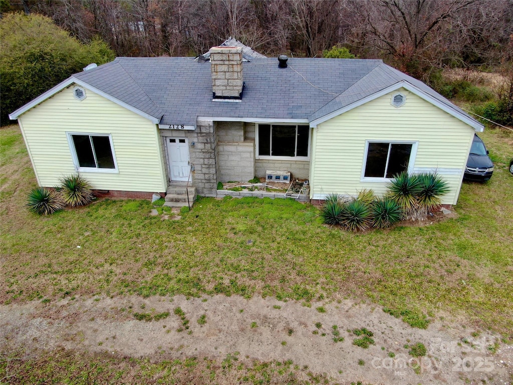 back of property featuring entry steps, stone siding, a lawn, and a chimney