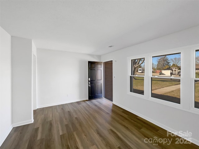 spare room with dark wood-style flooring, visible vents, and baseboards