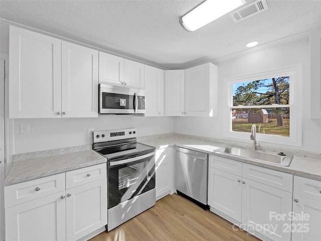 kitchen with stainless steel appliances, white cabinets, a sink, and visible vents