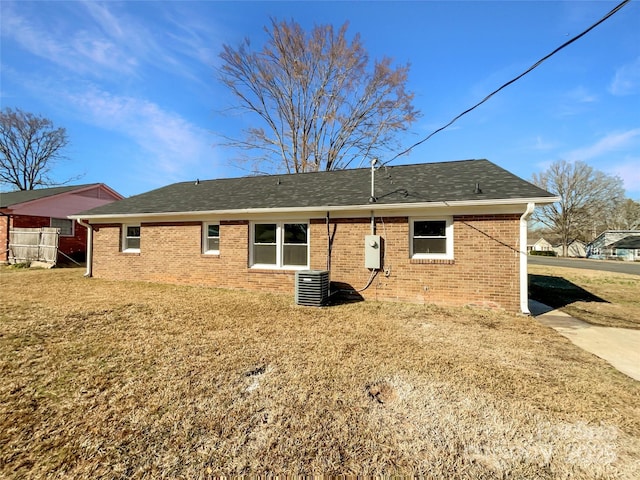 back of house with roof with shingles, brick siding, a lawn, and cooling unit