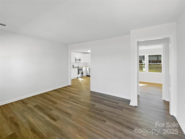 empty room with dark wood-type flooring, visible vents, and baseboards