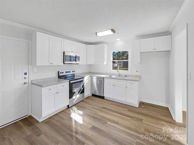 kitchen with a sink, white cabinets, light countertops, appliances with stainless steel finishes, and light wood-type flooring