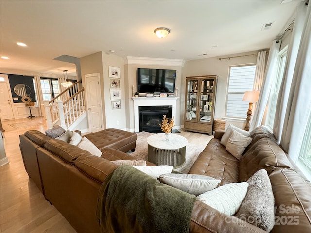 living room with stairway, a glass covered fireplace, visible vents, and light wood-style floors