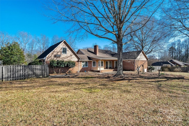 back of house featuring brick siding, a chimney, fence, and a yard