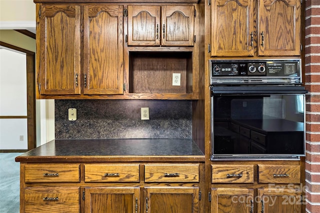 kitchen featuring brown cabinetry, dark countertops, oven, and backsplash