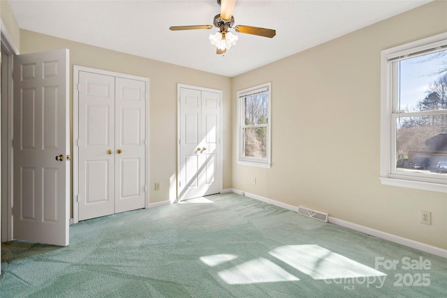 unfurnished bedroom featuring multiple closets, visible vents, a ceiling fan, carpet flooring, and baseboards