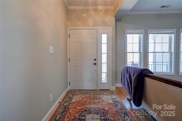 foyer with ornamental molding, light wood-type flooring, visible vents, and baseboards