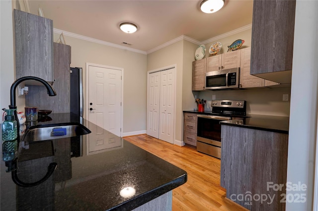 kitchen with light wood finished floors, visible vents, stainless steel appliances, crown molding, and a sink