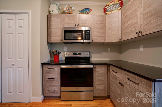 kitchen featuring appliances with stainless steel finishes, dark countertops, light wood-type flooring, and ornamental molding