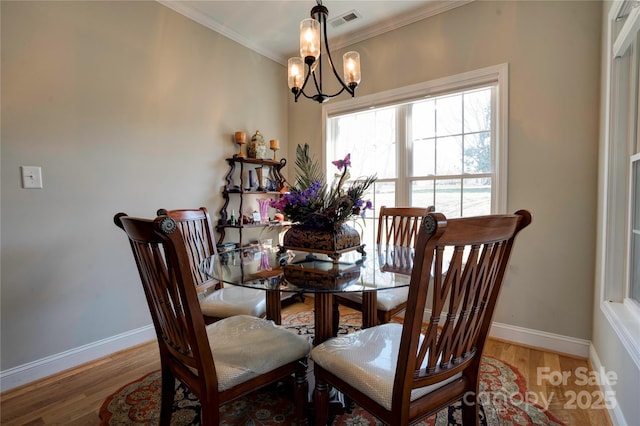 dining space with a notable chandelier, wood finished floors, visible vents, baseboards, and crown molding