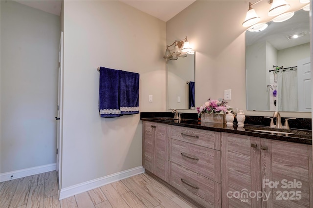 full bathroom with double vanity, baseboards, a sink, and wood finished floors