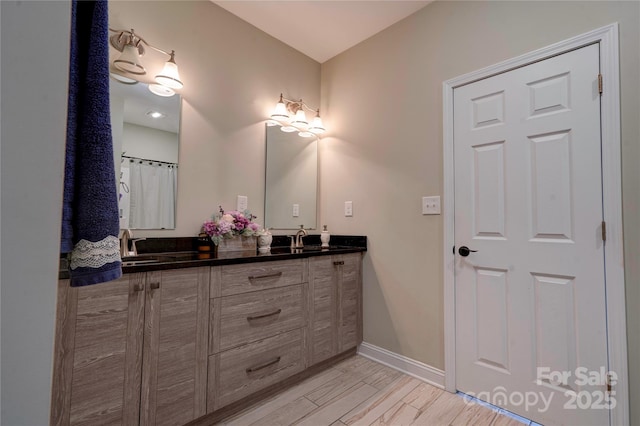 bathroom with a sink, double vanity, wood finished floors, and baseboards