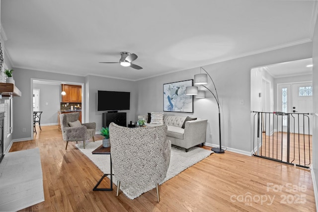 living area featuring light wood-style flooring, ornamental molding, baseboards, and a glass covered fireplace