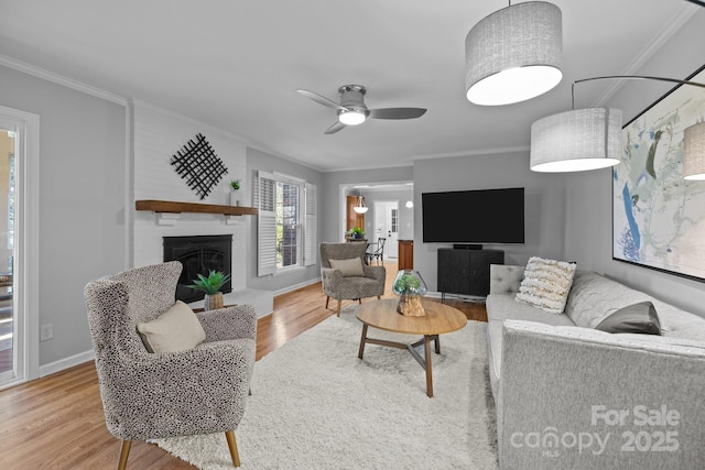 living area with baseboards, a ceiling fan, wood finished floors, crown molding, and a fireplace