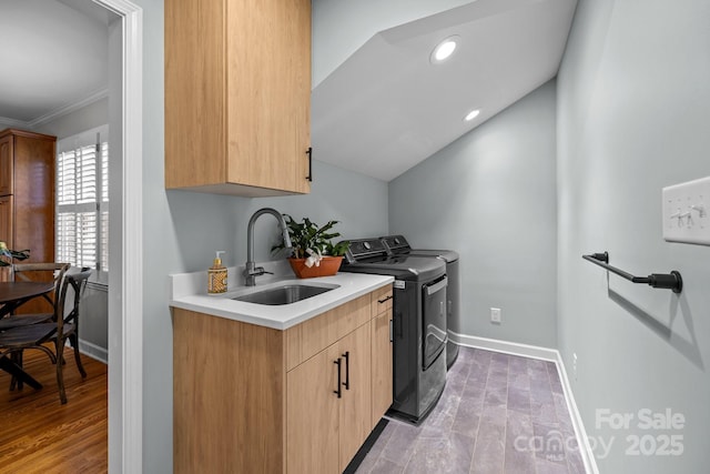 clothes washing area featuring cabinet space, light wood finished floors, baseboards, washing machine and clothes dryer, and a sink